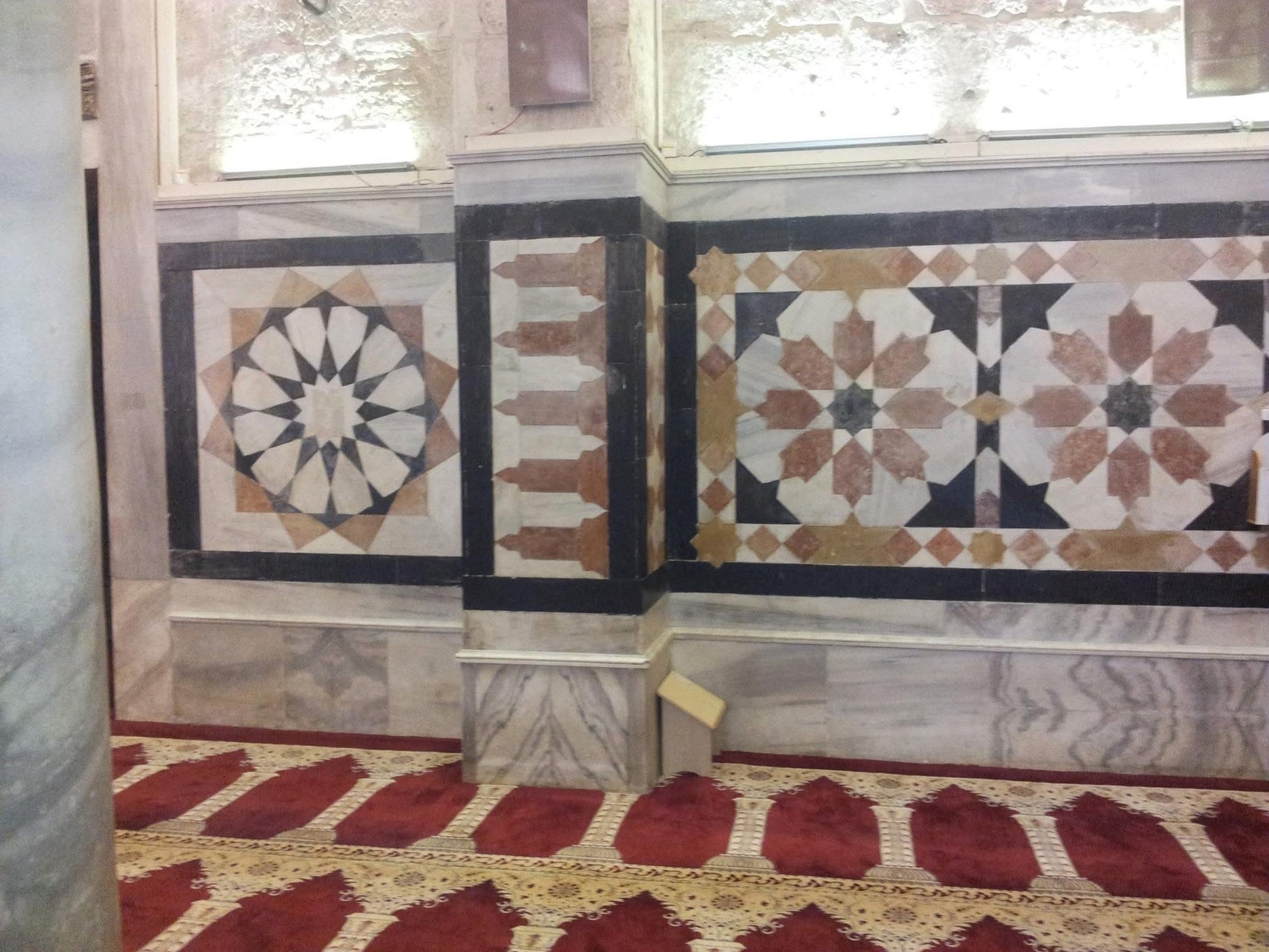 Decorative marble wall with intricate patterns and a red and gold carpet on the floor.